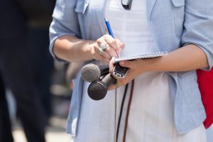 A legal journalist taking notes on a notepad at a live event with a microphone in her other hand